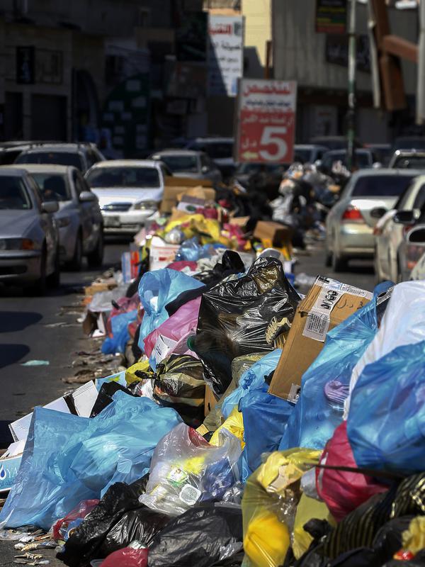 Kendaraan melintas di samping tumpukan sampah di sepanjang sisi jalan di Tripoli, ibukota Libya (30/9/2019). Truk sampah kota tidak lagi mengumpulkan sampah karena TPA utama kota ada di garis depan. (AFP Photo/Mahmud Turkia)