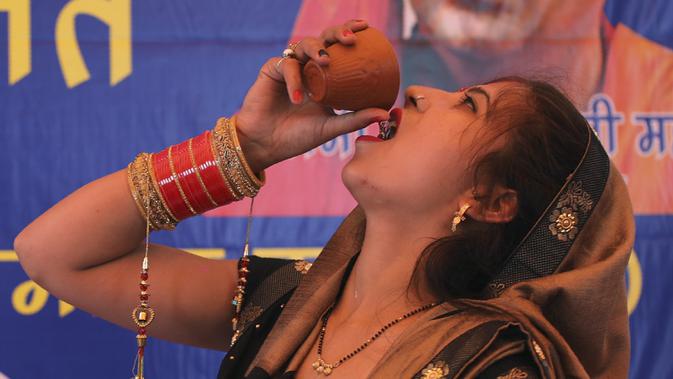 Seorang wanita Hindu India minum urine sapi selama acara yang diselenggarakan oleh kelompok agama Hindu untuk mempromosikan konsumsi urine sapi sebagai obat virus corona Covid-19 di New Delhi, India, Sabtu, (14/3/2020). (AP Photo/Altaf Qadri)