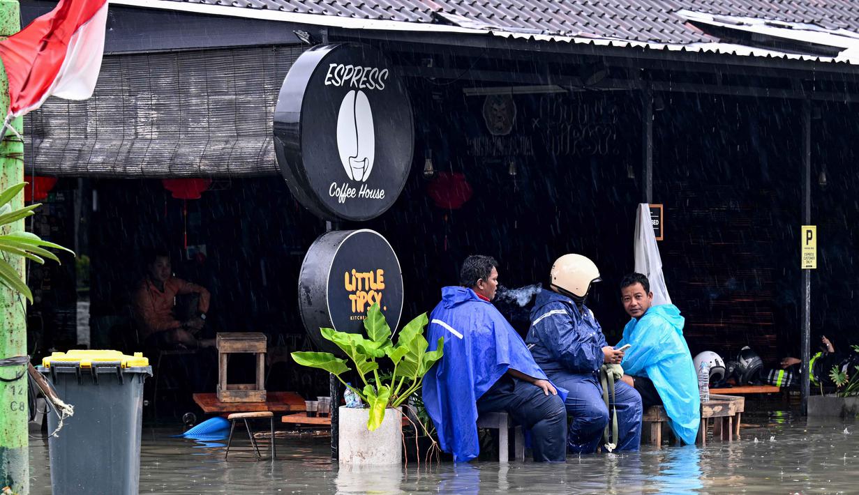 Sebagai upaya penanganan darurat, petugas Badan Penanggulangan Bencana Daerah (BPBD) bersama anggota TNI diterjunkan ke lokasi banjir. Tampak dalam foto, orang-orang duduk di sebuah kafe yang terendam banjir akibat hujan lebat di Legian Kuta, Denpasar, Bali, pada Selasa 24 Februari 2026. (SONNY TUMBELAKA/AFP)