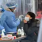 Petugas medis (tengah) mengambil sampel usap hidung dari seorang wanita di pusat pengujian virus corona COVID-19, Seoul, Korea Selatan, Rabu (16/2/2022). Kasus COVID-19 harian Korea Selatan meningkat tajam mencapai angka tertinggi baru yaitu lebih dari 90 ribu. (Jung Yeon-je/AFP)