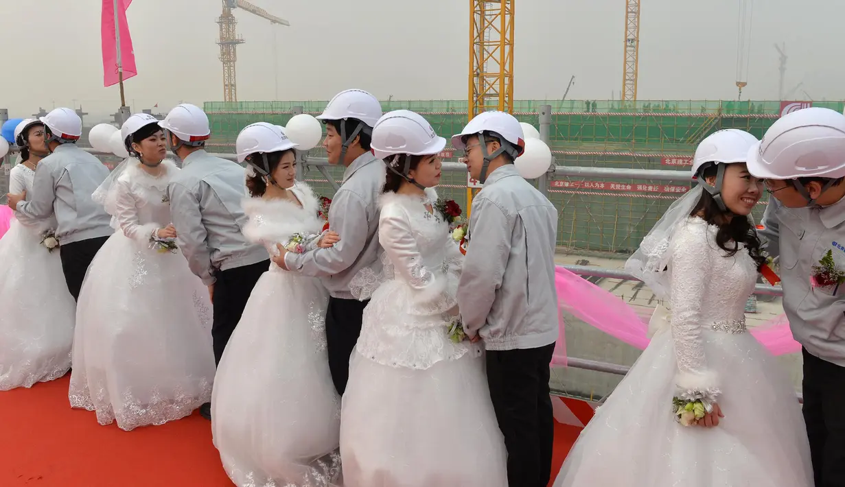 Pengantin pria dipersilahkan mencium pengantin wanita mereka usai upacara pernikahan, Beijing, Senin (12/12). Kelima pekerja ini kompak untuk menggelar upacara pernikahan di tempat proyek mereka bekerja yaitu sebuah bandara. (AFP PHOTO)