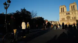 Orang-orang berhenti di depan Katedral Notre-Dame yang kembali membunyikan lonceng utamanya di Paris, Rabu (15/4/2020). Lonceng utama katedral kembali dibunyikan setelah satu tahun mengalami kebakaran yang sampai mengejutkan seluruh warga dunia. (AP/Christophe Ena)