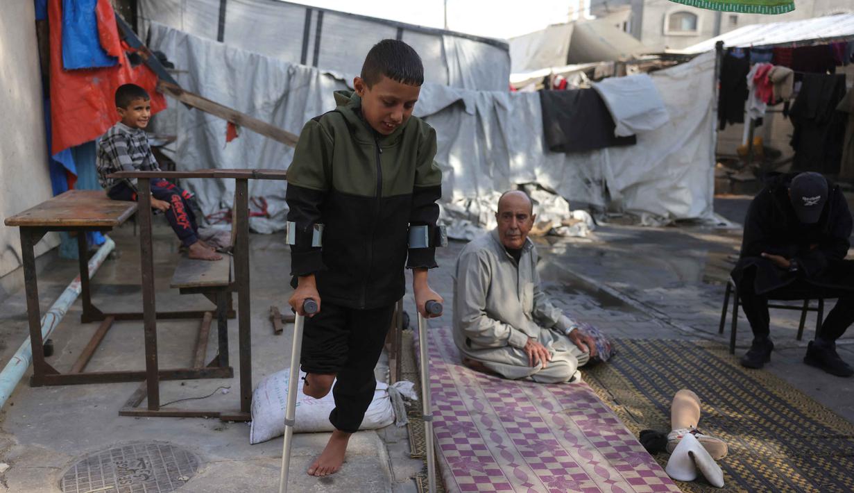 Saat ini, Rateb Mahmoud Qaliq, yang berasal dari desa Badui di Jalur Gaza utara, mengungsi dan tinggal bersama kakeknya di sebuah sekolah UNRWA di Deir al-Balah, Jalur Gaza tengah, yang berfungsi sebagai tempat penampungan. Tampak dalam foto, Rateb Mahmoud Qaliq bersama kakeknya di halaman sekolah UNRWA yang telah menjadi tempat penampungan bagi pengungsi Palestina di Deir al-Balah, di Jalur Gaza tengah, pada 3 Desember 2025. (Bashar Taleb/AFP)