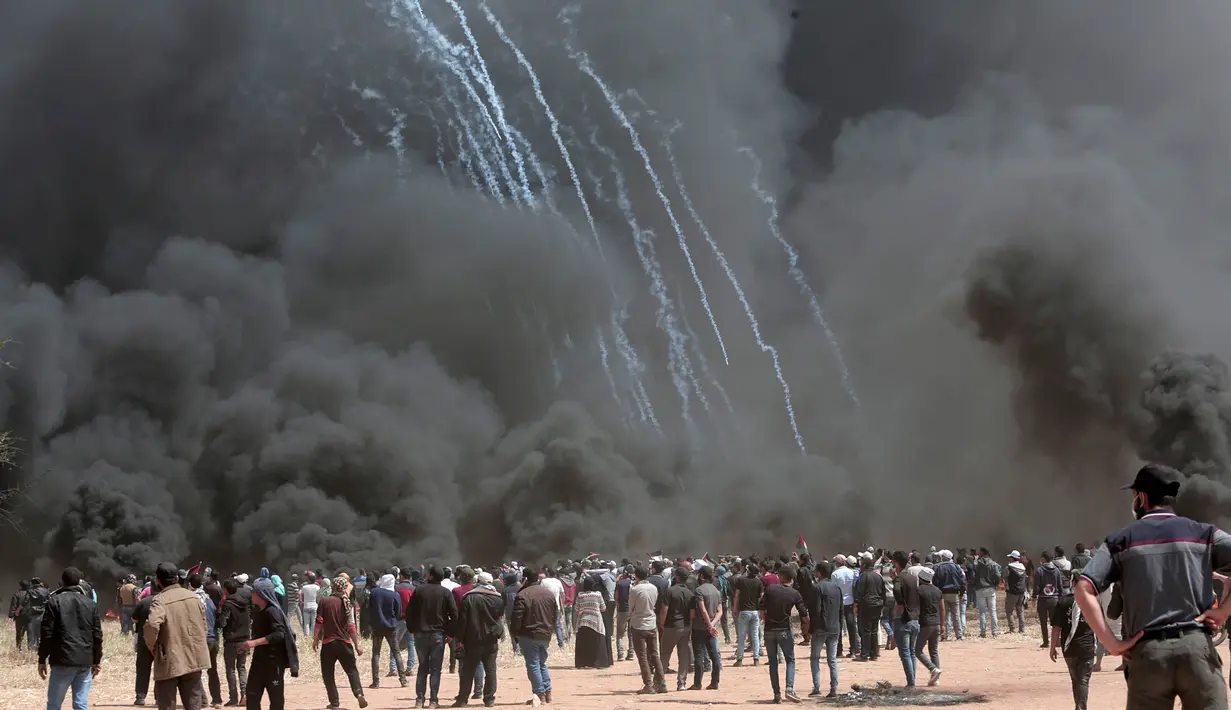Para pengunjuk rasa Palestina berkumpul di depan ban yang terbakar saat aksi protes di perbatasan Gaza dengan Israel, Jumat (6/4). Tentara terus menembakkan gas air mata dan peluru tajam selama aksi berlangsung. (AP Photo/Adel Hana)