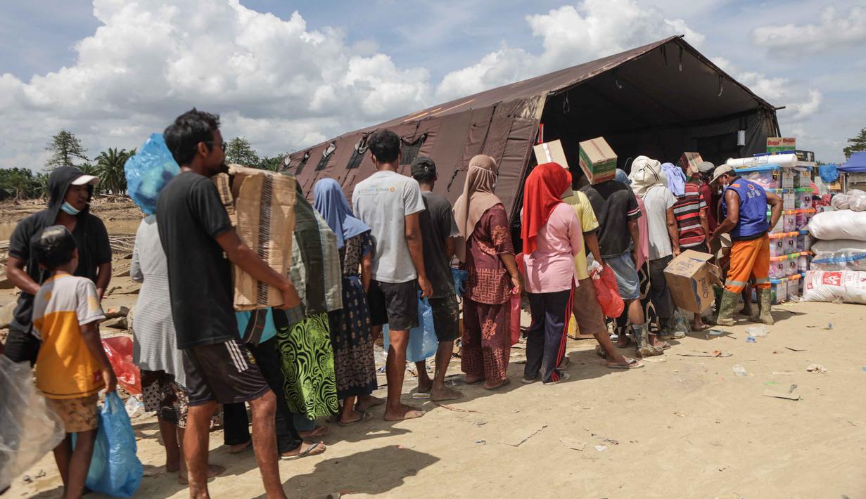 Warga pun masih kekurangan pasokan bahan pangan dan obat-obatan. Tampak dalam foto, warga mengantre untuk menerima pasokan makanan pokok dan air minum di pos logistik yang dibangun oleh warga setempat untuk menampung bantuan yang masuk, di desa Lintang Bawah di Aceh Tamiang, Sumatera Utara, pada Kamis 11 Desember 2025. (Aditya Aji/AFP)