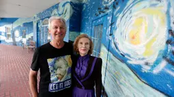 Sepasang suami istri, Nancy Nemhauser dan Lubomir Jastrzebski berpose dekat mural yang menghiasi rumah mereka di Mount Dora, Florida, 18 Juli 2018. Dekorasi The Starry Night pada rumah itu dinilai melanggar aturan kota tempat tinggalnya. (AP/John Raoux)