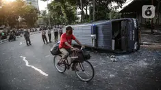 Seorang pengendara sepeda melintas dekat sebuah mobil polisi yang dirusak massa saat bentrok di kawasan Pejompongan, Jakarta, Rabu (7/10/2020). (Liputan6.com/Faizal Fanani)