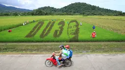 Pengendara motor melintasi sawah yang menampilkan karya seni wajah Presiden Filipina Rodrigo Duterte dengan huruf D U dan nomor 3, sebuah permainan kata dari nama Presiden "DU30", di Kota Los Banos, Manila Selatan, Kamis (6/10). (REUTERS/Romeo Ranoco)