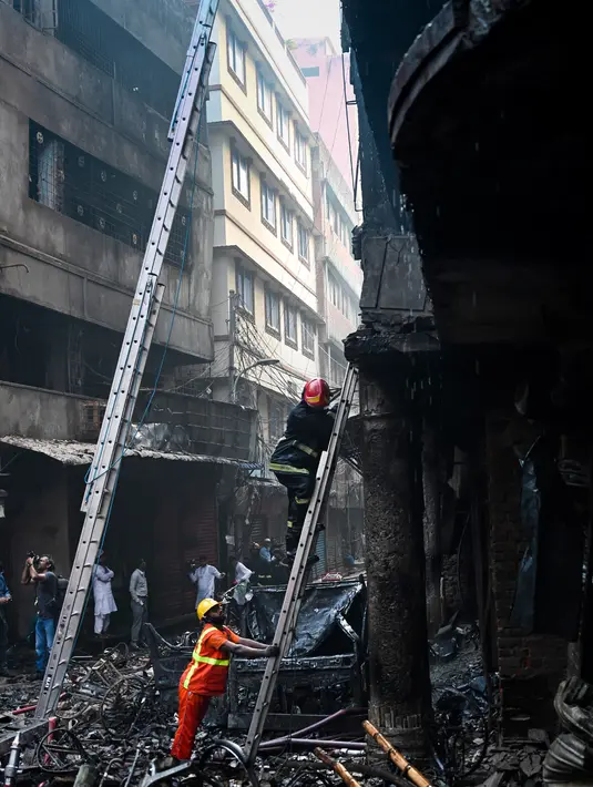 Petugas pemadam kebakaran menggunakan tangga berusaha menaiki gedung apartemen setelah kebakaran di Dhaka (21/2). Setidaknya 69 orang tewas dalam kebakaran besar tersebut. (AFP Photo/Munir Uz Zaman)