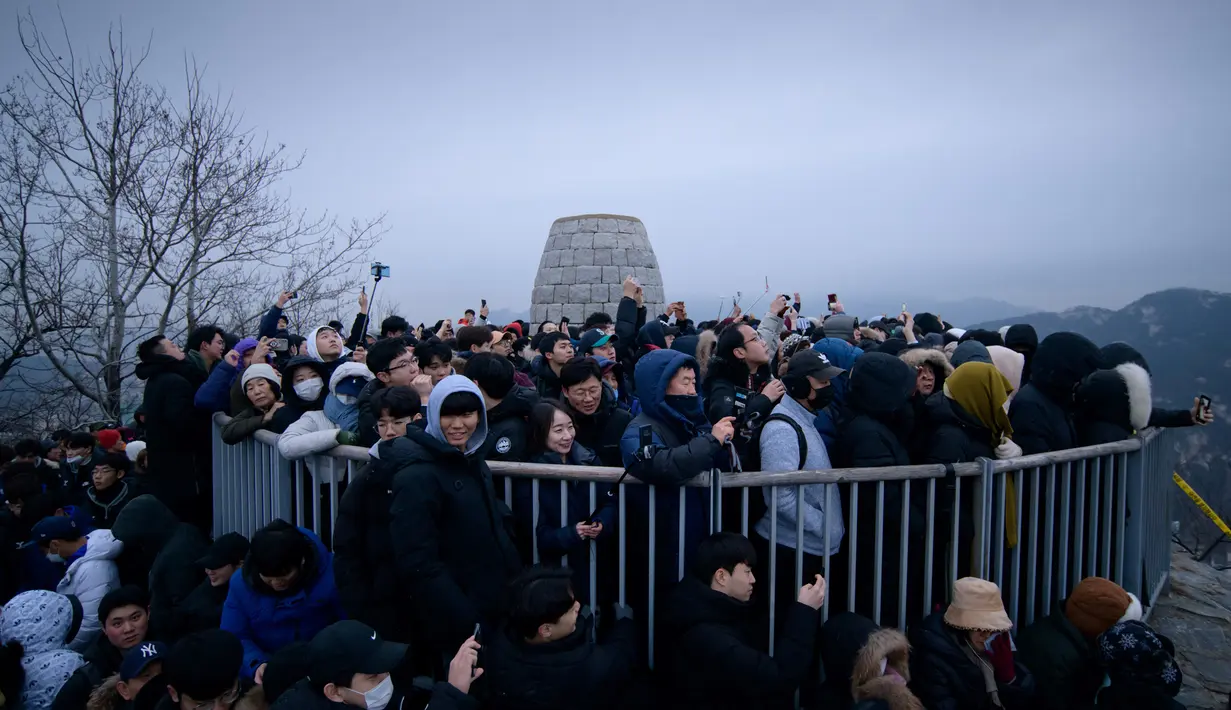 Orang-orang berkumpul di sudut pandang yang menghadap ke cakrawala kota untuk menyaksikan matahari terbit pertama tahun baru, meskipun dalam kondisi mendung, di Seoul, Korea Selatan (1/1/2020). (AFP/Ed Jones)