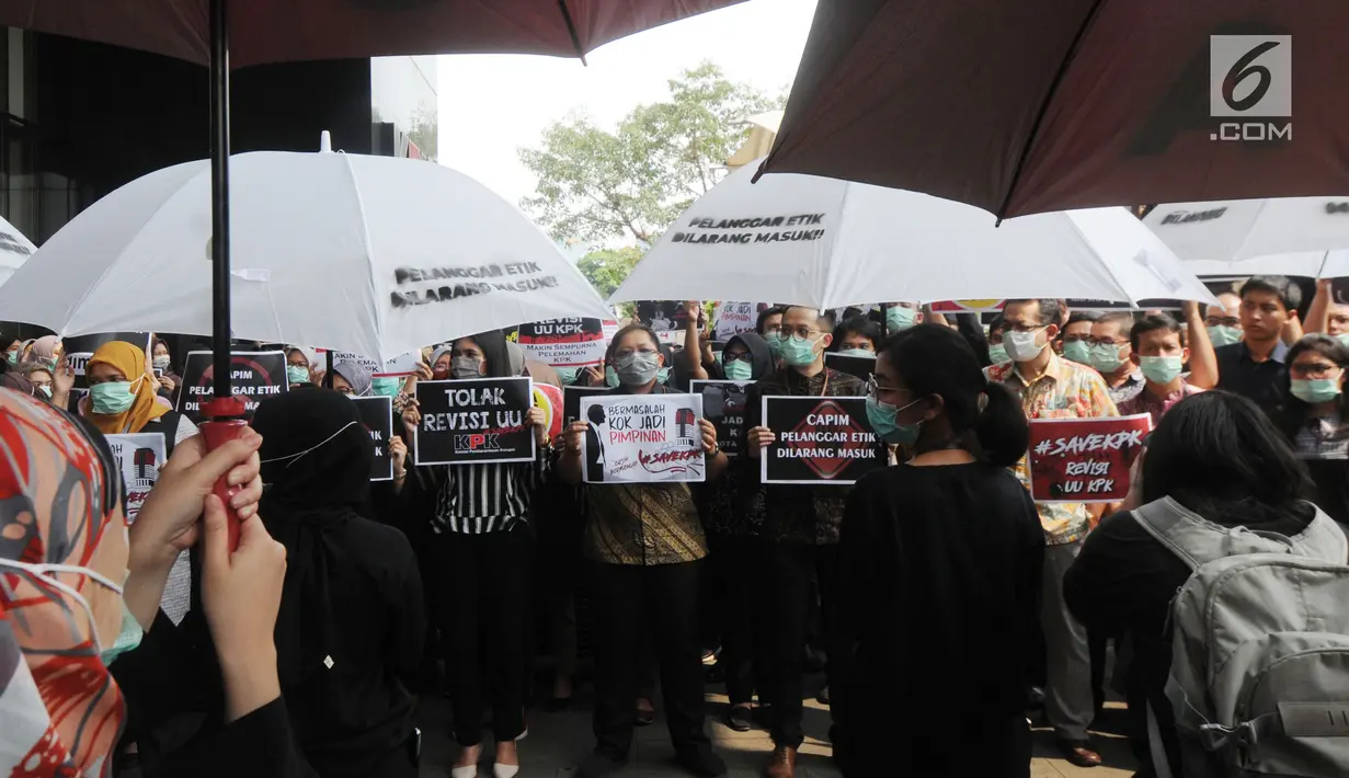 Pegawai KPK membawa poster saat menggelar aksi di Lobi Gedung KPK, Kuningan, Jakarta, Jumat (6/9/2019). Dalam aksi menolak revisi UU KPK tersebut, mereka mengenakan baju serba hitam lengkap dengan masker penutup mulut dan memasang KPK Lines di sekitar pintu masuk. (merdeka.com/Dwi Narwoko)