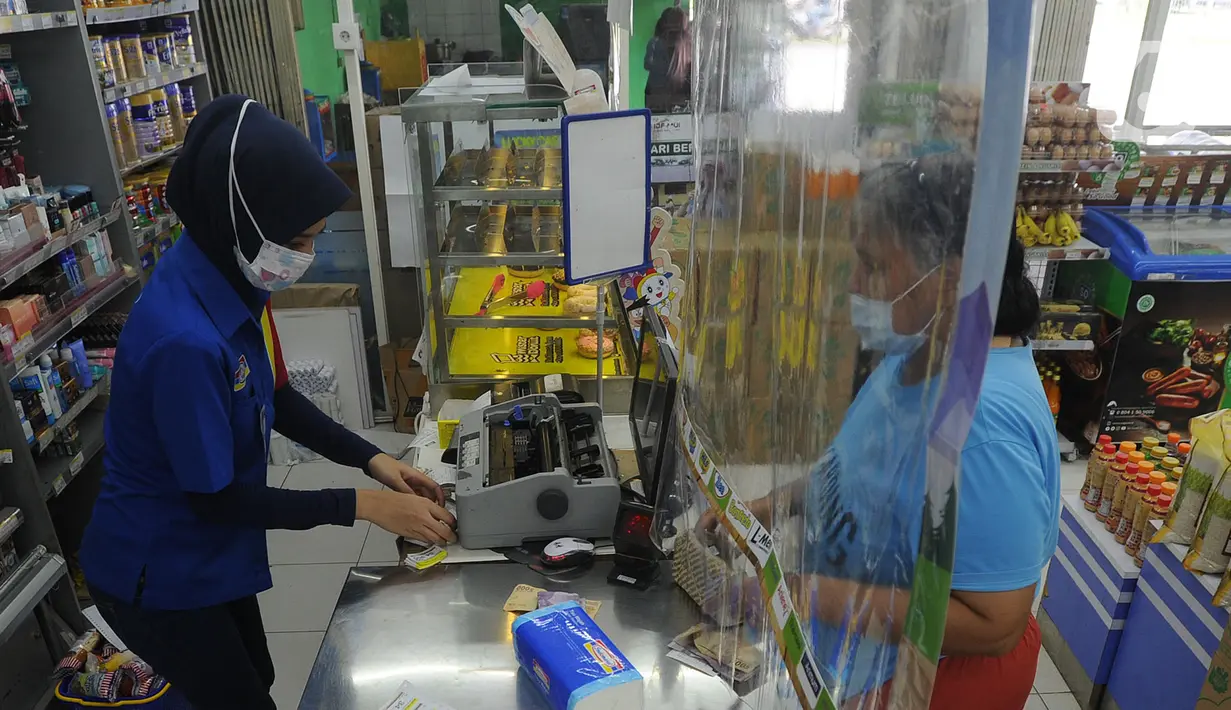 Pekerja melayani pembeli dari balik plastik pembatas pada sebuah minimarket di kawasan Cinere, Depok, Jawa Barat, Rabu (8/4/2020). Penggunaan plastik pembatas tersebut bertujuan untuk mengantisipasi penyebaran virus corona atau COVID-19 sebagai bentuk social distancing. (merdeka.com/Arie Basuki)