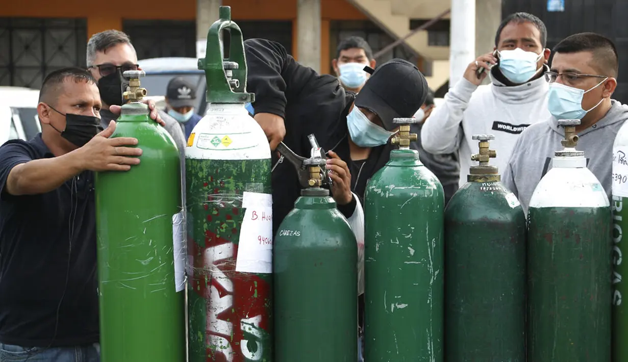 Para pria menyesuaikan tangki oksigen kosong saat antre menunggu toko isi ulang di Callao, Peru, Senin (25/1/2021). Di tengah pandemi COVID-19, beberapa orang mengatakan mereka telah antre sehari sebelumnya untuk menjadi yang pertama saat toko buka. (AP Photo/Martin Mejia)