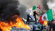Pengunjuk rasa melambaikan bendera dari atas mobil yang rusak saat bentrok dengan penegak hukum di jalan-jalan di sekitar gedung federal selama protes setelah operasi imigrasi federal di Los Angeles, California, Amerika Serikat pada 8 Juni 2025. (RINGO CHIU/AFP)