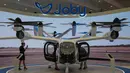 Adalah Joby Aviation Inc. perusahaan asal Amerika Serikat, tengah melakukan rangkaian uji terbang untuk pesawat taksi udara berbasis baterai mereka di Margham menuju Bandara Internasional Al Maktoum, Uni Emirat Arab. Tampak dalam foto, seorang wanita mengambil foto taksi udara Dubai yang dipamerkan pada Pameran Udara Dubai, Uni Emirat Arab, Selasa 18 November 2025. (AP Photo/Altaf Qadri)