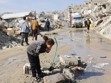 Warga Palestina yang mengungsi hidup di tengah reruntuhan rumah dan bangunan yang hancur akibat serangan militer Israel selama lebih dari dua tahun di wilayah Gaza, minum air dari keran umum, di kamp pengungsi Jabalia, di Jalur Gaza utara pada Sabtu 17 Januari 2026. Gedung Putih membentuk Komite Nasional untuk Administrasi Gaza (National Committee for the Administration of Gaza/NCAG) dan Dewan Perdamaian Gaza. (Omar AL-QATTAA/AFP)