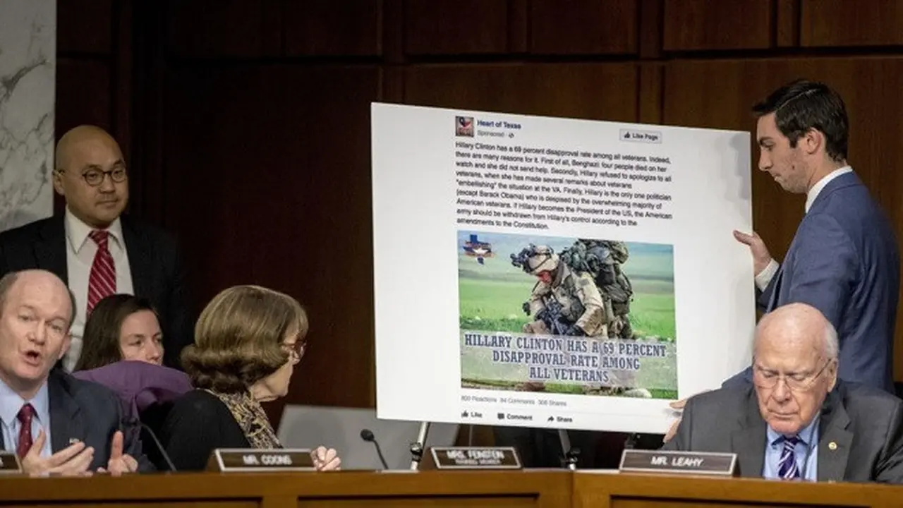 Senator Chris Coons (kiri) berbicara sementara seorang asistennya menayangkan sebuah poster yang menampilkan contoh iklan Facebook yang menyesatkan dalam sidang dengar pendapat Komite Hukum di Capitol Hill (AP)