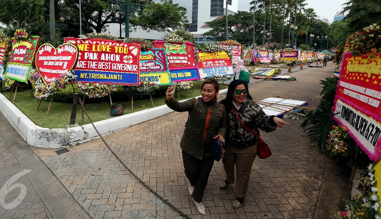 Warga berfoto di depan karangan bunga untuk Basuki T Purnama dan Djarot Sjaiful Hidayat di Balai Kota Jakarta, Selasa (25/4). Karangan bunga tersebut terus bertambah berisi simpati warga kepada Ahok-Djarot pascapilkada DKI 2017. (Liputan6/Johan Tallo)