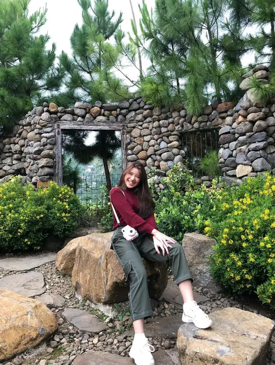 Gaya Tiara Andini dengan turtleneck top warna merah maroon dan celana kargo hitam, serta sneakers putih ini bisa memberikan kesan sporty casual pada penampilan kamu. (Instagram/tiaraandini).