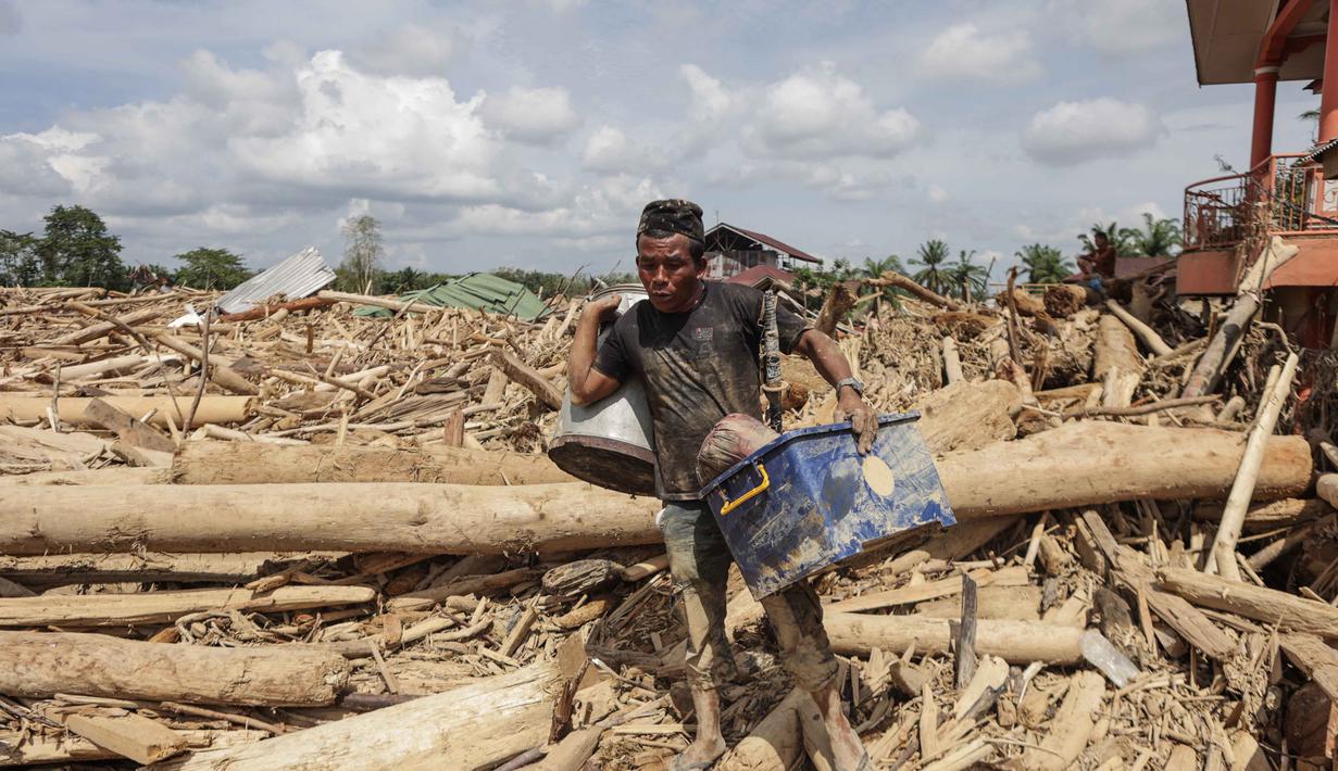 Proses pemulihan masih terus berjalan, meski agak lama lantaran infrastruktur yang terputus dan lumpur yang tak kunjung surut. Tampak dalam foto, seorang pria membawa barang-barang miliknya yang berhasil diselamatkan dari tumpukan pohon tumbang akibat banjir bandang, di desa Lintang Bawah, Aceh Tamiang, Sumatera Utara, pada Kamis 11 Desember 2025. (Aditya Aji/AFP)