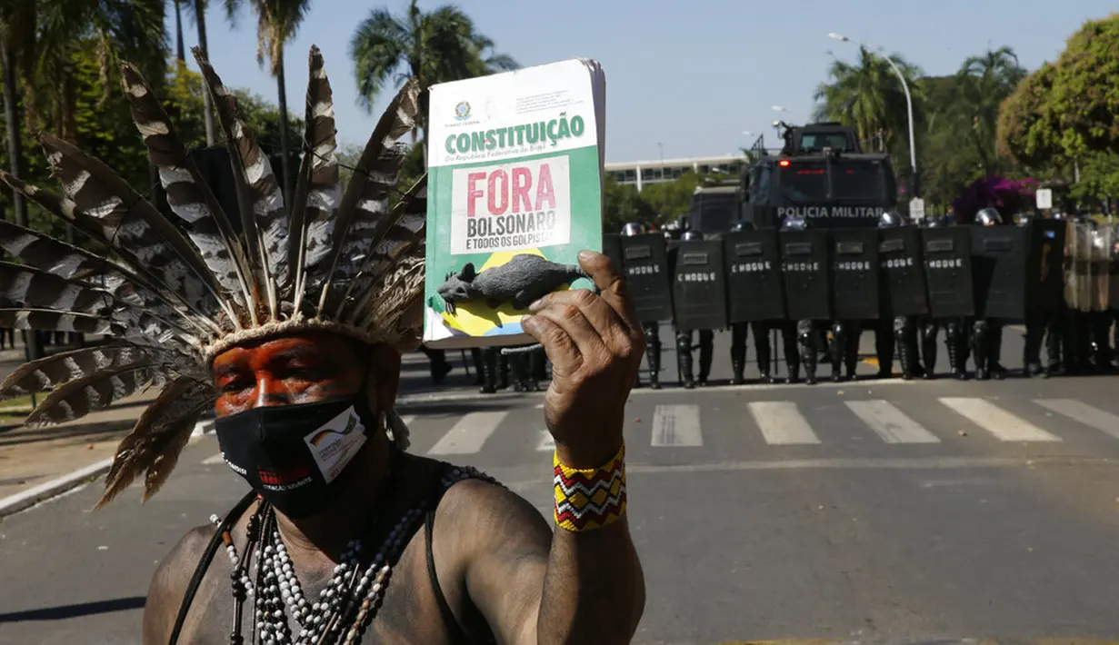 Seorang pengunjuk rasa memegang salinan konstitusi yang dicap dengan pesan yang berbunyi dalam bahasa Portugis; "Bolsonaro Out" saat demo menentang RUU Reformasi Agraria di luar Kongres di Brasilia, Brasil, Selasa (22/6/2021). (AP Photo/Eraldo Peres)