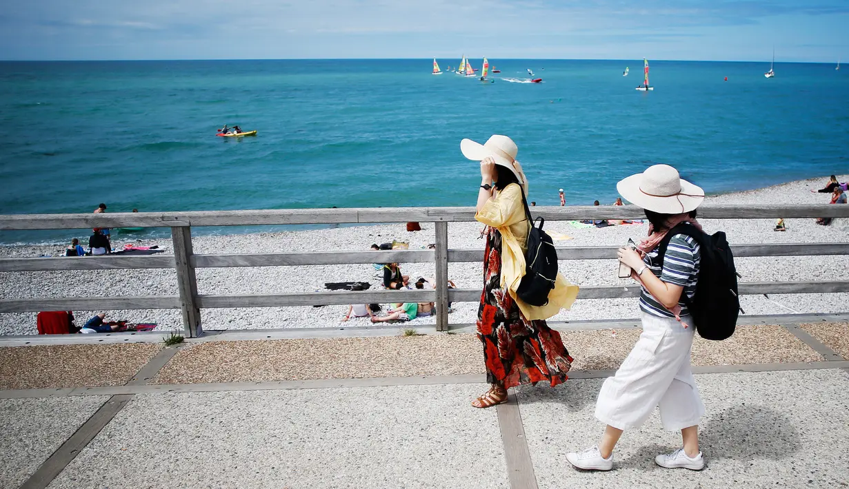 Wisatawan berjalan di sepanjang kawasan pantai di Etretat, Prancis barat laut (17/7). Etretat dikenal akan tebing-tebingnya, termasuk tiga lengkungan alami dan "jarum" di dekatnya. (AFP Photo/Charly Triballeau)