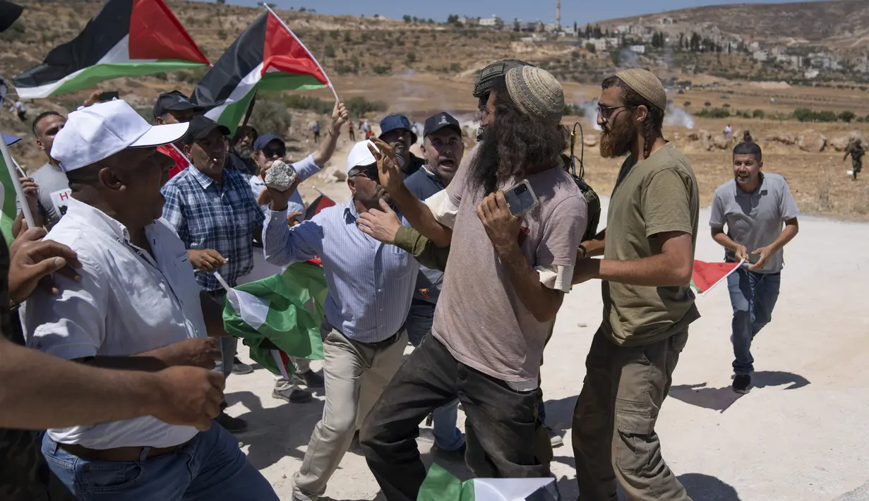 Pemukim Israel bentrok dengan pengunjuk rasa Palestina yang memblokir jalan yang melewati Desa Mughayer, Tepi Barat, utara Ramallah, 29 Juli 2022. Warga Palestina yang memprotes aktivitas permukiman Israel memblokir jalan utama dan bentrok dengan pemukim Israel, sementara tentara menembakkan gas air mata untuk membubarkan mereka. (AP Photo/Nasser Nasser)