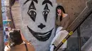 Seorang wanita berpose dekat lukisan wajah Joker di tangga di kawasan Bronx, New York, 23 Oktober 2019. Tangga yang terletak tepat di West 167th Street itu menjadi buruan wisatawan, terutama para penggemar film Joker yang ingin berfoto. (Don Emmert / AFP)