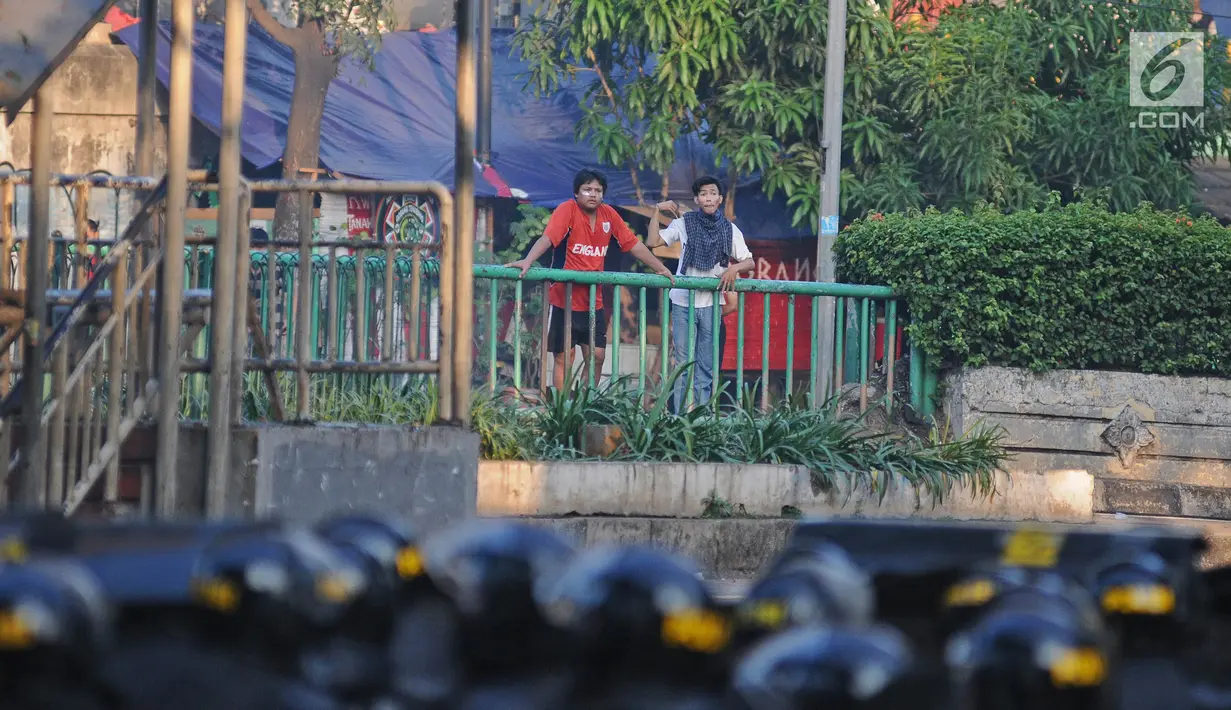 Dua orang pria melihat bentrok antara polisi dan massa aksi di kawasan Tanah Abang, Jakarta, Rabu (22/5/2019).  Beberapa kelompok massa menggunakan benda-benda keras hingga mercon untuk menahan laju petugas keamanan. (Liputan6.com/Herman Zakharia)