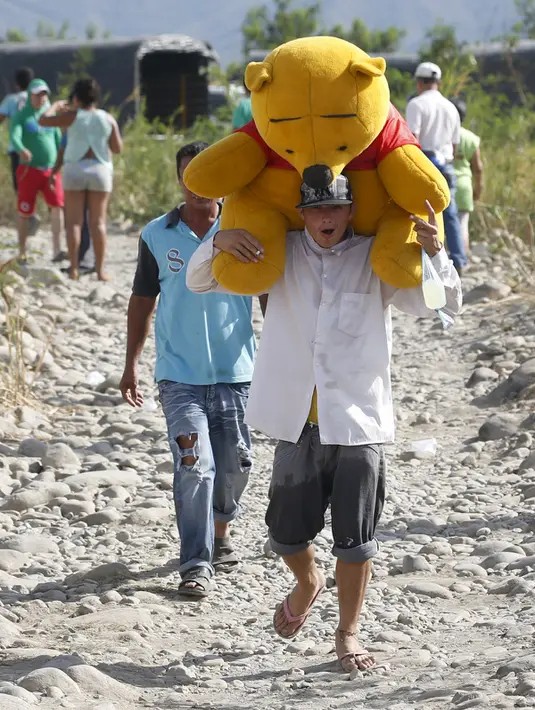 Seorang warga Kolombia membawa boneka beruang saat melintasi perbatasan dengan Venezuela di sungai Tachira (25/8/2015). Pada hari ini (26/8/) kedua negara dilaporkan akan memulai perundingan mengenai masalah ini. (REUTERS/Jose Miguel Gomez)