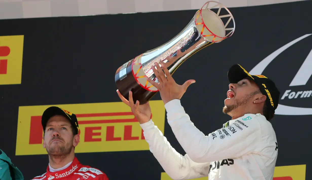 Pembalap Mercedes, Lewis Hamilton merayakan kemenangannya pada balapan F1 GP Spanyol di atas podium Sirkuit Catalunya, Minggu (14/5). Hamilton yang start dari posisi pole menyelesaikan 66 lap dengan gemilang. (AP Photo/Emilio Morenatti)