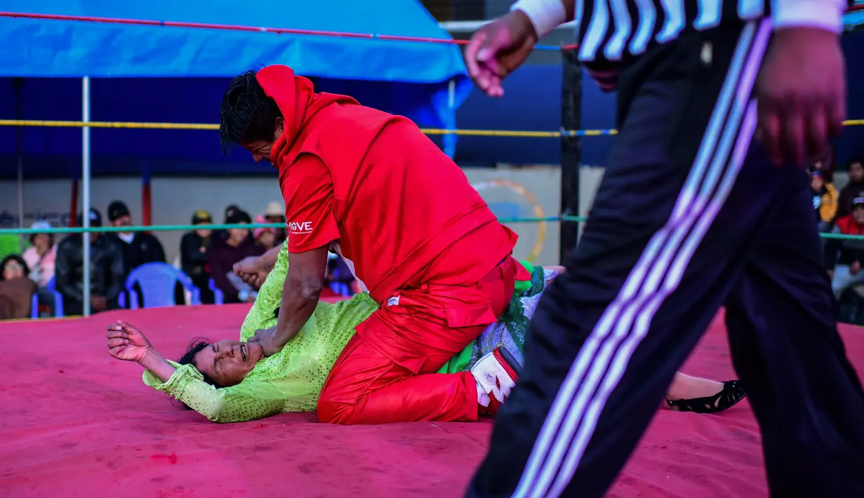 Pegulat Bolivia, Lidia Flores dikunci oleh lawannya pegulat pria di atas ring gulat di El Alto, pada 24 November 2019. Di Bolivia ada sebuah atraksi gulat yang diperankan perempuan dengan menggunakan busana khas warga Bolivia. (Ronaldo SCHEMIDT / AFP)