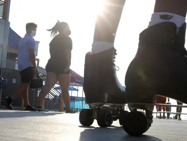 Orang-orang yang mengenakan masker berjalan dekat sepatu roda di Santa Monica, California, Kamis (3/9/2020). Permintaan sepatu roda di Amerika Serikat mengalami peningkatan tajam untuk mencari aktivitas di luar ruangan di tengah pembatasan sosial akibat corona Covid-19. (Mario Tama/Getty Images/AFP)