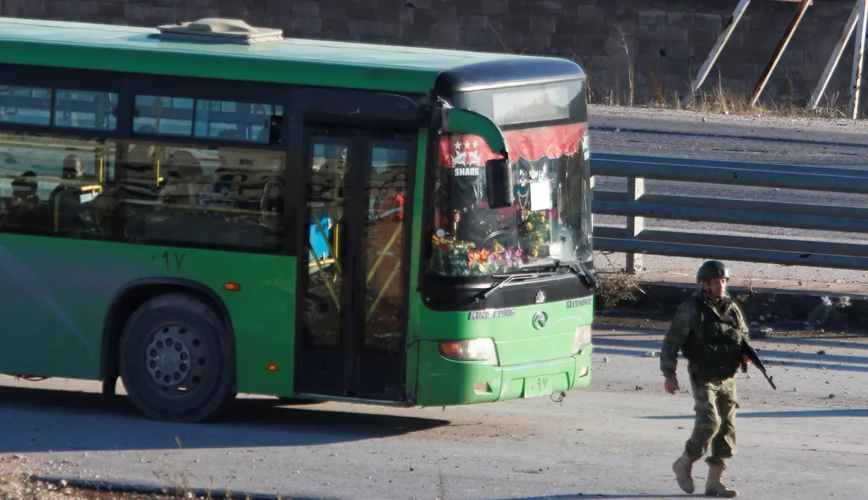 Sebuah bus yang digunakan untuk mengevakuasi warga sipil melewati seorang anggota pasukan Presiden Suriah Bashar al-Assad, meninggalkan wilayah yang dikuasai pemberontak di Aleppo, Suriah, Kamis (15/12). (REUTERS/Omar Sanadiki)