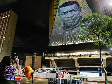 Seorang wanita mengambil gambar mendiang pemain sepak bola Pele yang ditampilkan pada Gedung Federasi Industri Sao Paulo di Sao Paulo, Brasil, 29 Desember 2022. Pele yang menghabiskan sebagian besar kariernya bersama Santos FC telah meninggal di Sao Paulo. (AP Photo/Marcelo Chello)