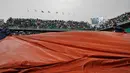 Pekerja stadion menarik penutup lapangan usai pertandingan perempat final Perancis Terbuka ditunda di stadion Roland Garros, Paris (6/6). Pertandingan antara Rafael Nadal dan Diego Schwartzman sempat ditunda karena hujan. (AP/Christophe Ena)