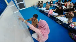 Seorang guru mengajar murid tanpa menggunakan meja dan kursi sekolah, di SDN Bojong Nangka 02, Kabupaten Bogor, Jawa Barat, Kamis (16/2/2023). Sudah lebih dari dua pekan, murid-murid di tiga ruang kelas  menerapkan kegiatan belajar mengajar beralas karpet karena belum tersedianya bangku dan meja. (merdeka.com/Arie Basuki)