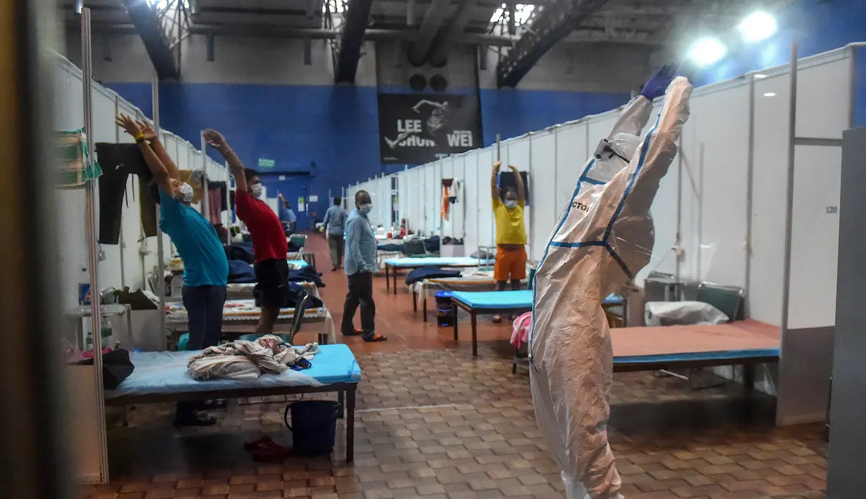 Seorang dokter yang mengenakan setelan Alat Pelindung Diri memberikan instruksi kepada pasien saat melakukan yoga di dalam bangsal di kompleks olahraga Commonwealth Games (CWG) Village yang sementara diubah menjadi pusat perawatan Covid-19 di New Delhi, India, Kamis (16/7/2020). (Money SHARMA / AFP)