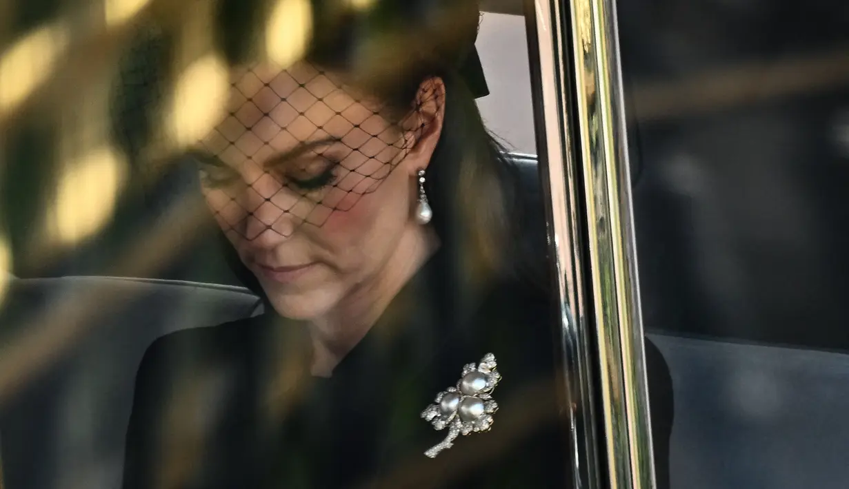 Kate Middleton berada di dalam mobil saat menghadiri prosesi persemayaman Ratu Elizabeth II di Westminster Hall di London (14/9/2022). Kate Middleton yang mendapat gelar baru sebagai Princess of Wales memakai bros berlian dan mutiara berbentuk daun. (AFP/Marco Bertorello)