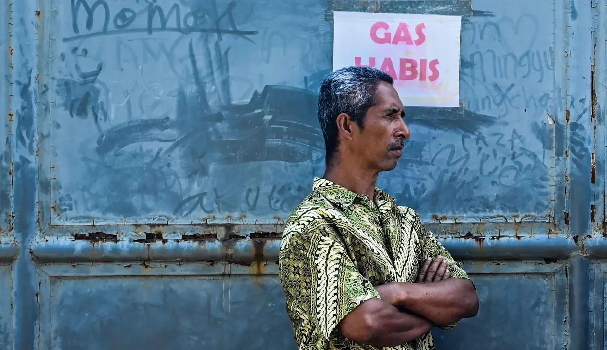 Kepastian kelancaran distribusi gas ini terkait upaya pemulihan kondisi daerah yang terdampak bencana banjir dan longsor di Sumatera. Tampak dalam foto, seorang pria berdiri di samping poster bertuliskan "Gas Habis" di sebuah SPBU setelah banjir bandang di Banda Aceh pada Rabu 17 Desember 2025. (CHAIDEER MAHYUDDIN/AFP)