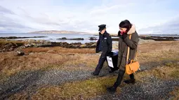 Margaret Byrne (kiri) berjalan mengawal pejabat ketua, Majella Harkin saat mendistribusikan kotak suara di Inishfree, Irlandia, Kamis (25/2). Pulau terpencil ini hanya terdapat empat orang yang memiliki hak pilih. (REUTERS/Clodagh Kilcoyne)
