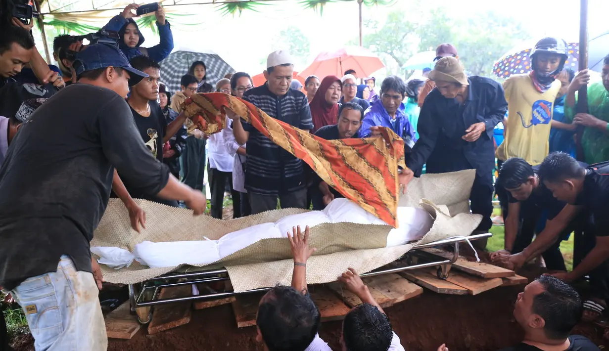 Suasana hujan tak kunjung reda ketika jenazah dikeluarkan dari ambulan yang membawanya. Dengan peralatan payung seadanya, untuk menutupi jenazah. Para pelayat juga menggunakan jas hujan menutupi tubuhnya dari guyuran hujan. (Adrian Putra/Bintang.com)