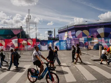 Pejalan kaki berjalan di dekat situs Paralimpiade Place de la Concorde yang ditutupi terpal "Paris 2024" menjelang ajang Paralimpiade 2024 di paris, Rabu (21/8/2024). (Dimitar DILKOFF / AFP)