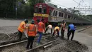 Kereta Commuter Line melintas di sebelah para pekerja yang sedang melakukan perawatan rutin rel kereta api di Manggarai, Jakarta, Selasa (11/7). (Liputan6.com/Helmi Afandi)