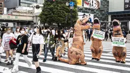 Aktivis kelompok hak hewan PETA mendesak orang untuk menjadi vegan selama protes di Tokyo, Jepang, Rabu (6/10/2021). Dalam aksinya, para aktivis mengenakan kostum dinosaurus. (CHARLY TRIBALLEAU/AFP)