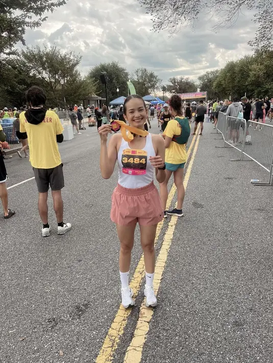 Senyum bahagia Enzy Storia dengan medali yang baru saja diraih setelah menyelesaikan lari maraton 21,5 K. Sedangkan sang suami memberikan dukungan dari jauh. [Instagram/enzystoria]