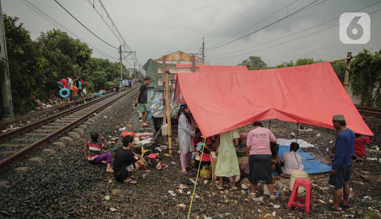 Pengungsi banjir mendirikan tenda di jalur rel kereta commuterline Tangerang-Duri di Kembangan Baru, Jakarta, Jumat (3/1/2020). Jalur rel yang nonaktif sementara karena banjir dimanfaatkan warga sekitar untuk mendirikan tenda darurat karena rumah mereka masih terendam. (Liputan6.com/Faizal Fanani)