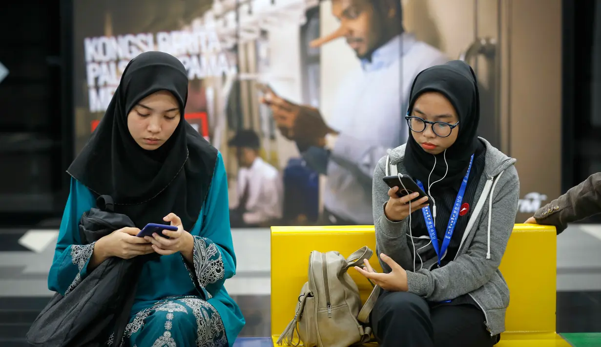 Penumpang menunggu kedatangan kereta dengan latar belakang iklan larangan penyebaran hoax atau berita bohong di Stasiun Kereta Kuala Lumpur, Malaysia, Senin (2/4). Pemerintah Malaysia mengesahkan UU Antihoax jelang Pemilu. (AP Photo/Vincent Thian)