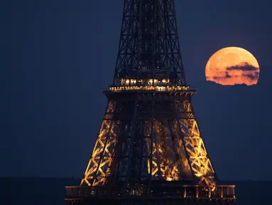 Foto yang diambil di Paris pada 23 April 2024 ini menunjukkan bulan purnama di bulan April, yang memiliki julukan pink moon atau bulan merah muda, terlihat di belakang Menara Eiffel. (Stefano RELLANDINI / AFP)