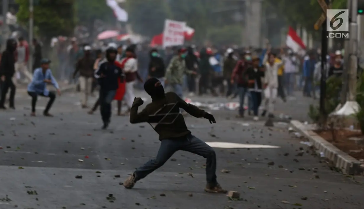 Seorang peserta aksi melempar batu ke arah polisi yang membentuk barikade dengan tameng di sekitaran Gedung DPR RI, Jakarta, Senin (30/9/2019). Kericuhan pecah lantaran massa yang kebanyakan terdiri dari pelajar tersebut berusaha masuk ke area depan DPR. (Liputan6.com/Johan Tallo)